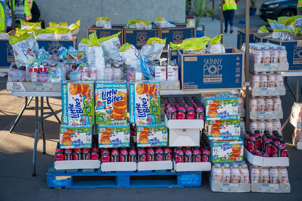 A vibrant display of various snack foods and beverages stacked on pallets, showcasing products like popcorn and flavored drinks at a community event.