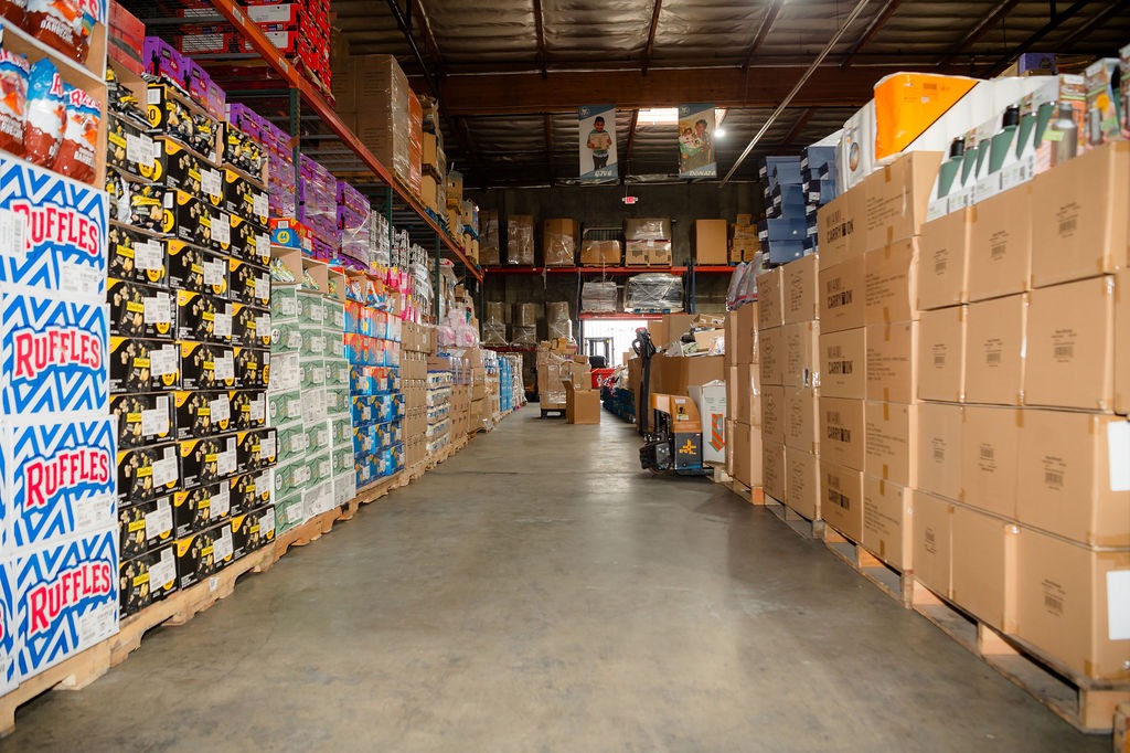 A wide aisle in a warehouse lined with colorful boxes of snacks and beverages, showcasing inventory organization and storage methods.
