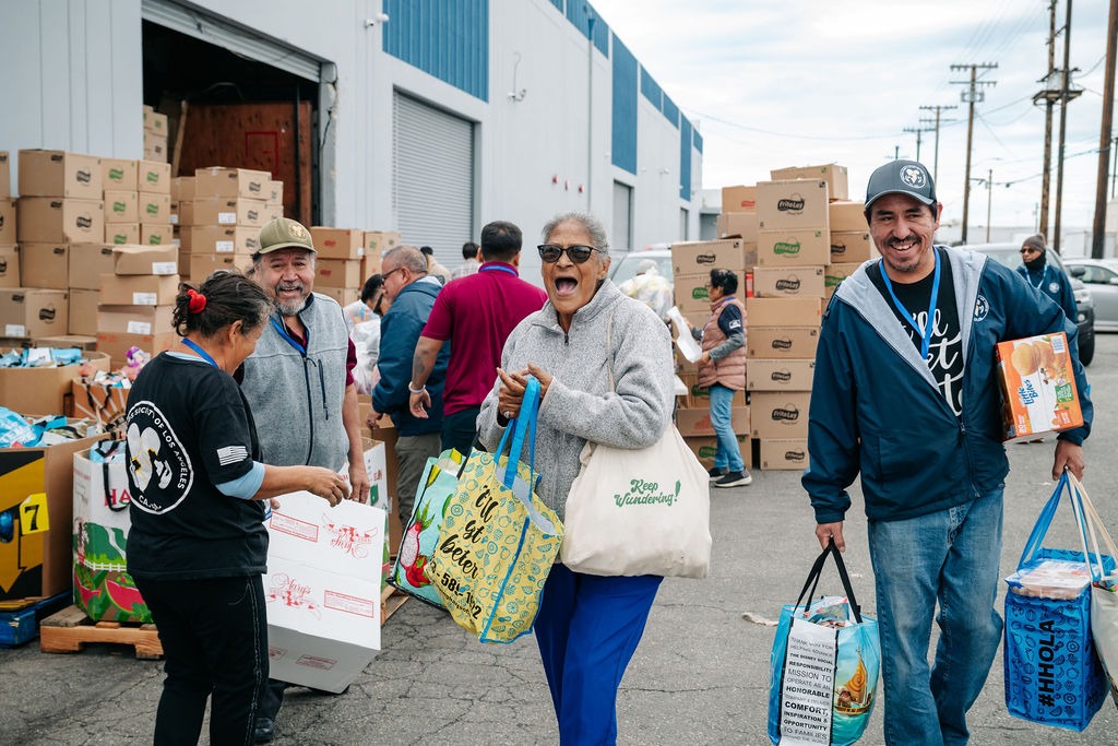 Community members joyfully receive supplies outside a food distribution center, showcasing a spirit of solidarity and support during a giveaway event.